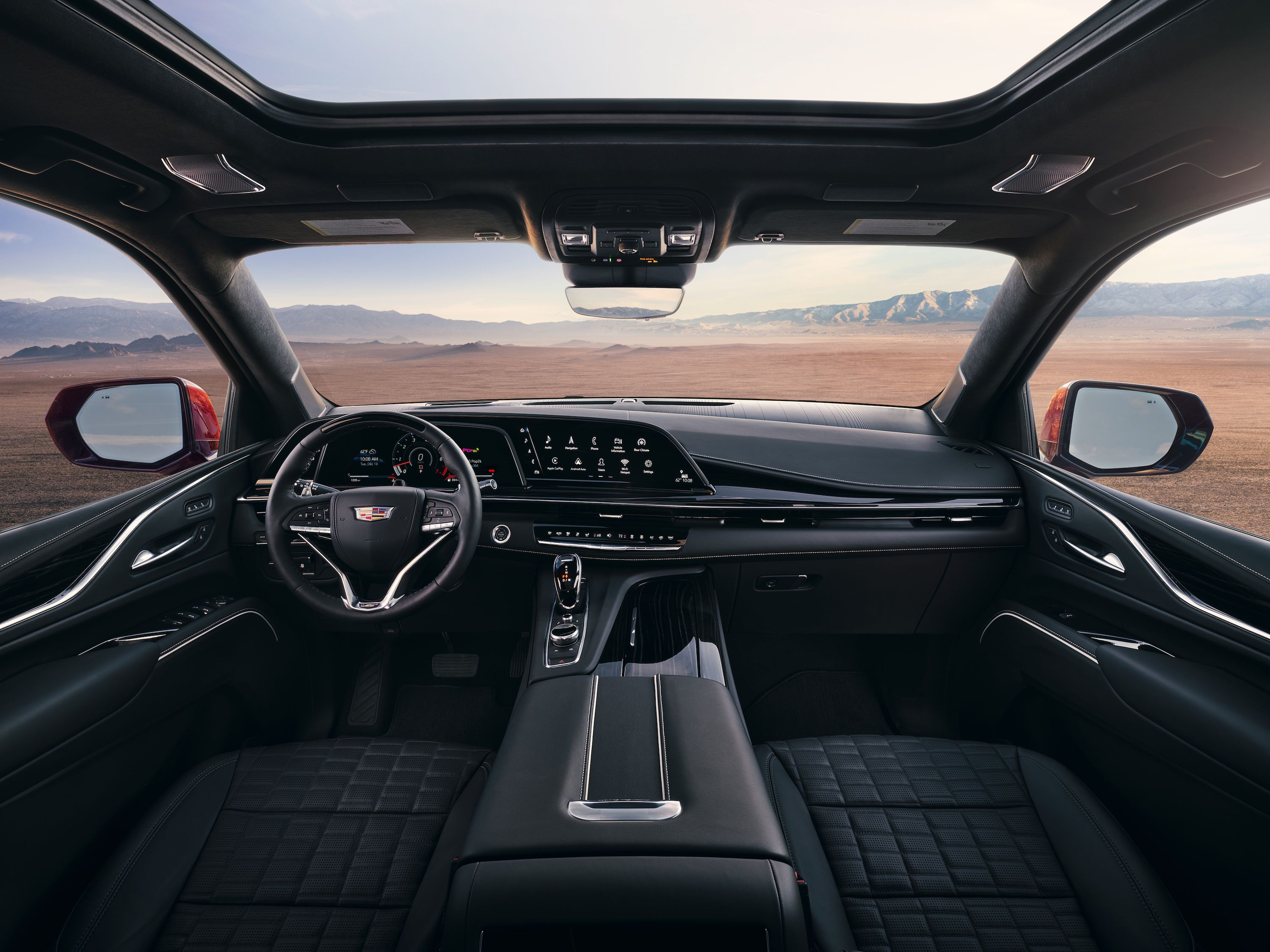 A car with the dashboard and steering wheel in front of an open window.