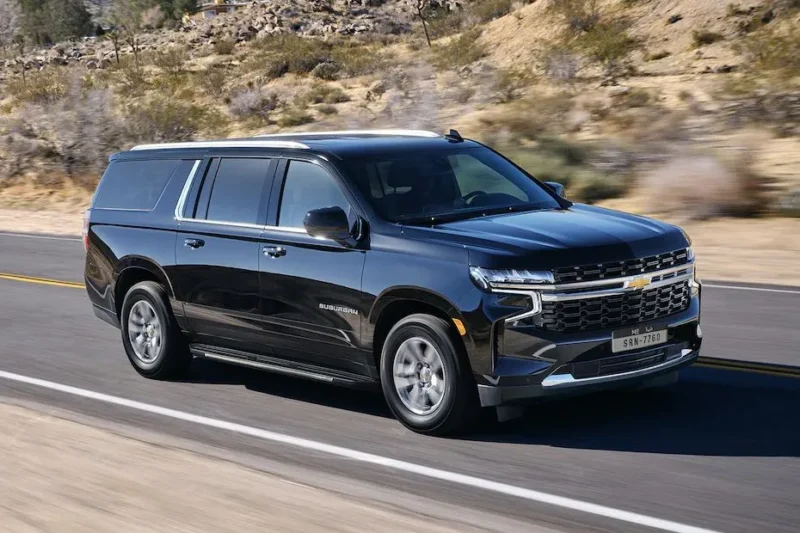 A black suv driving down the road near some rocks.